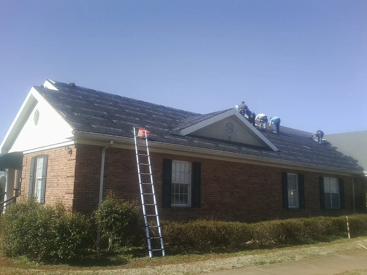 Crew tearing shingles off a brick ranch roof with a ladder set — Metal Roof Repair work by our crew in Abbottstown