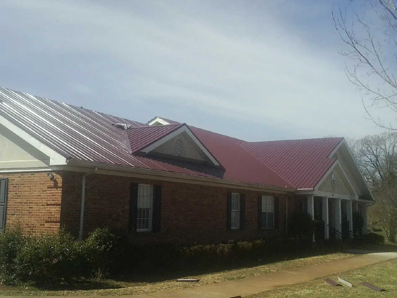 Red metal roof with gabled entries on a long brick building, from a Hail Damage Roof Repair job in Abbottstown