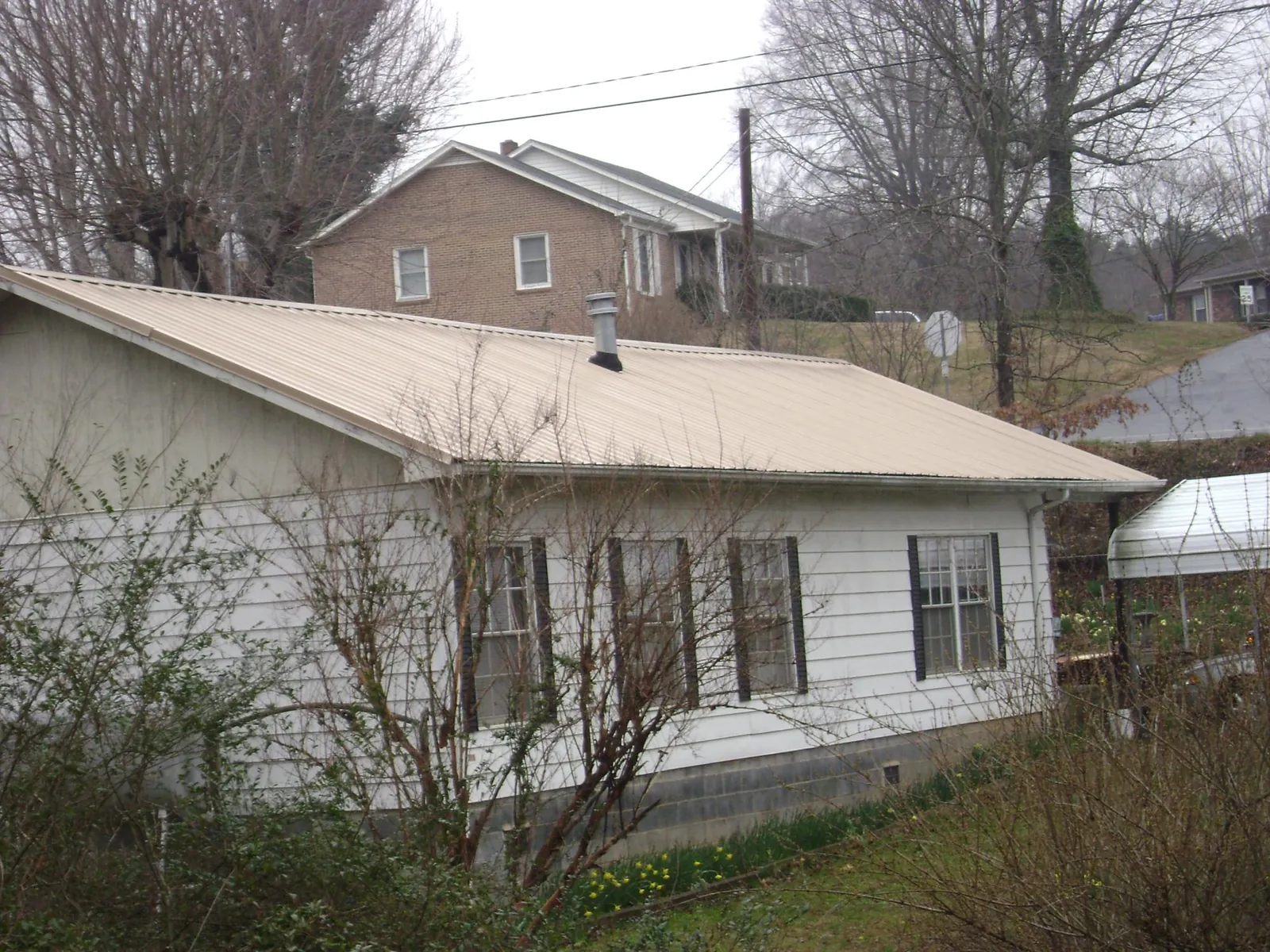 Tan metal roof on a white sided house set into a hillside — Commercial Roofing by Roofing Brothers in Abbottstown
